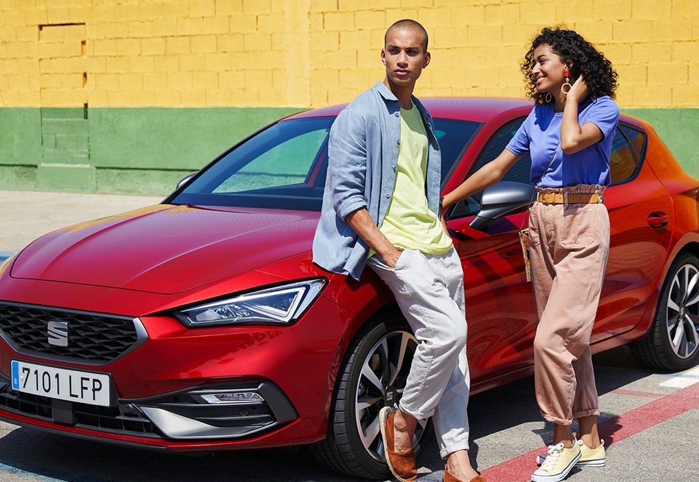 Twee personen die tegen een rode SEAT Leon aan leunen