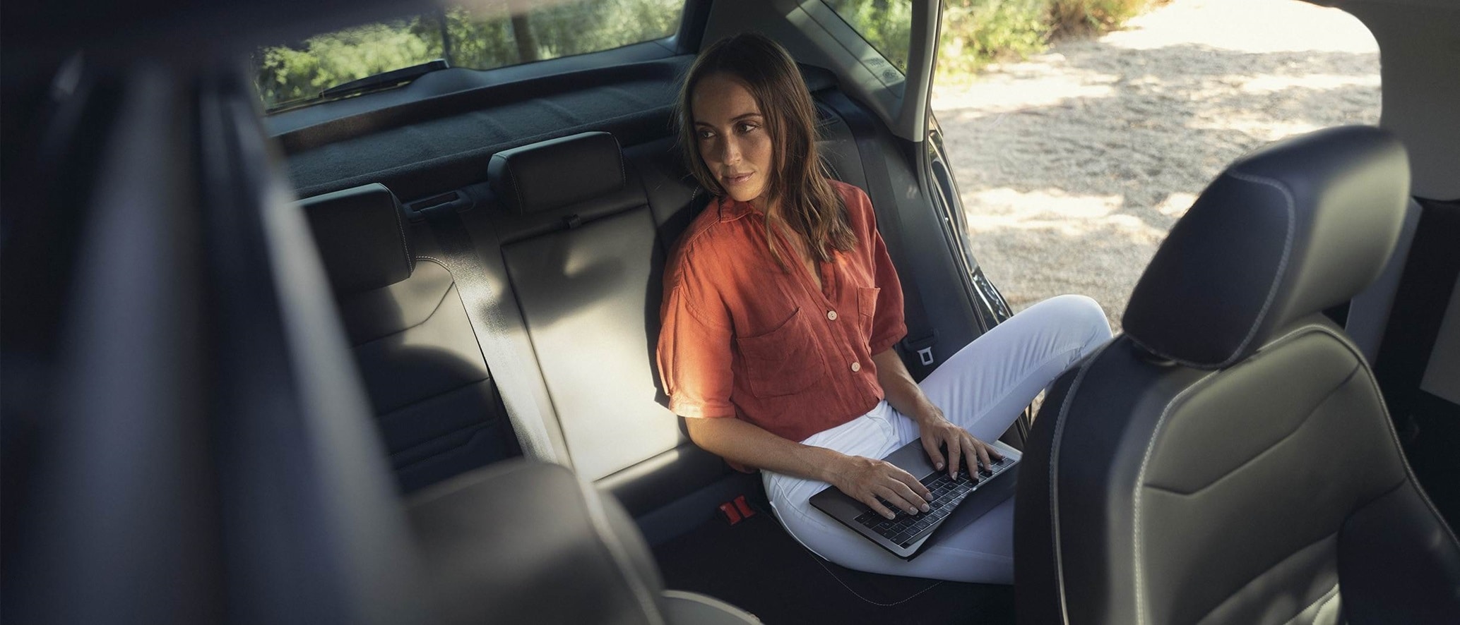 Vrouw zit op de achterbank van een SEAT met laptop op schoot