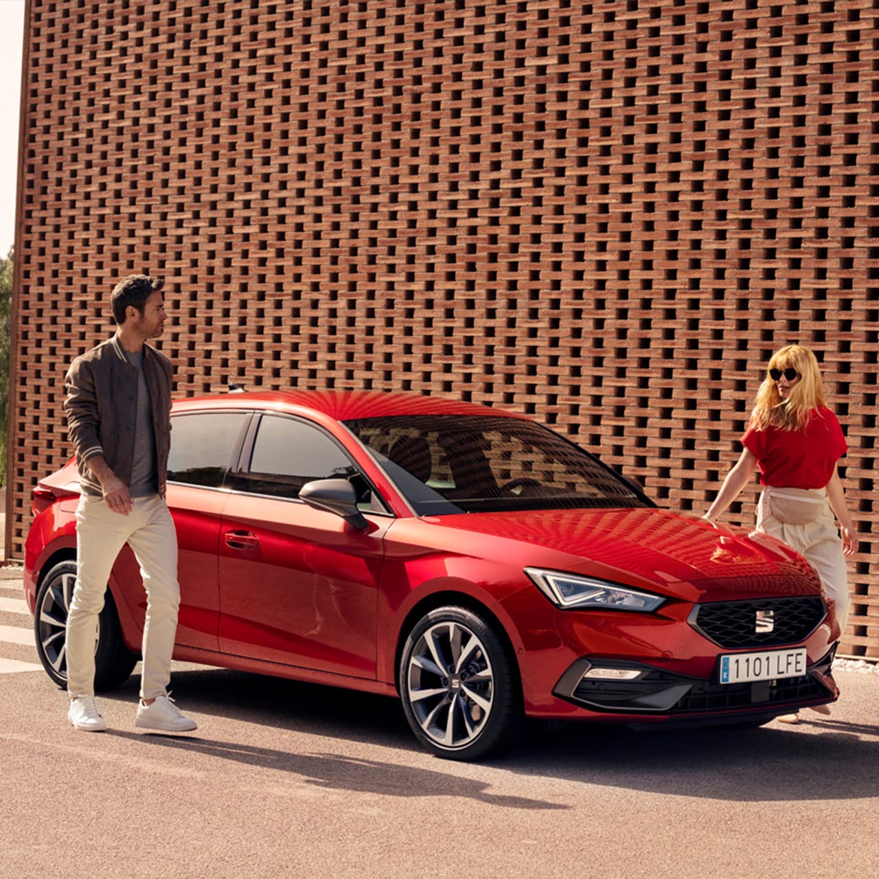 SEAT Leon FR mild hybrid hatchback in Desire Red met een man en een vrouw die rondom de auto lopen