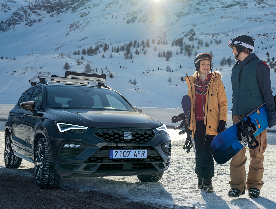 SEAT Ateca met allesdrager erop gemonteerd, met ernaast 2 personen in ski kleren