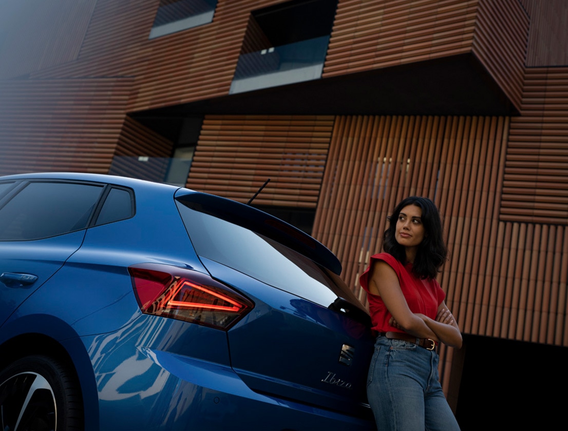 Vrouw in rode top die leunt tegen blauwe SEAT Ibiza