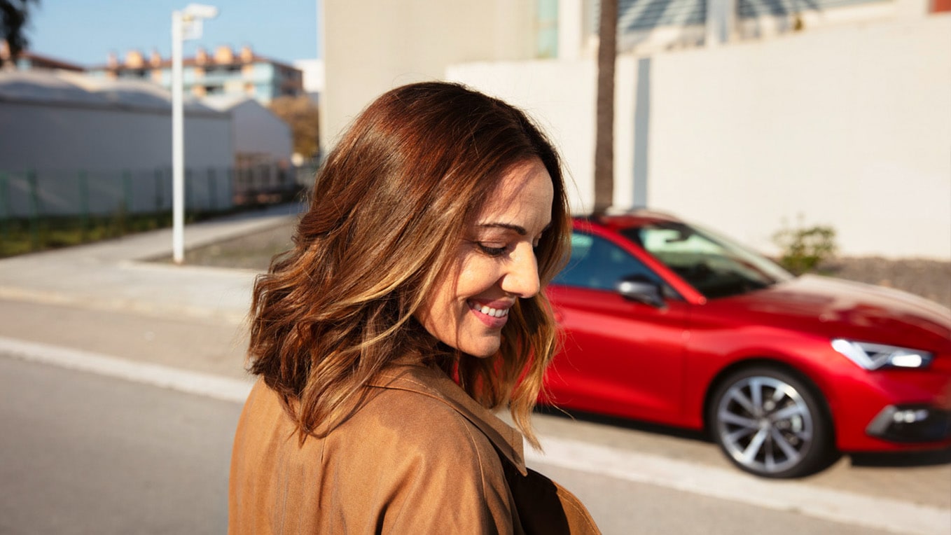 Glimlachende vrouw met op de achtergrond een rode SEAT Leon