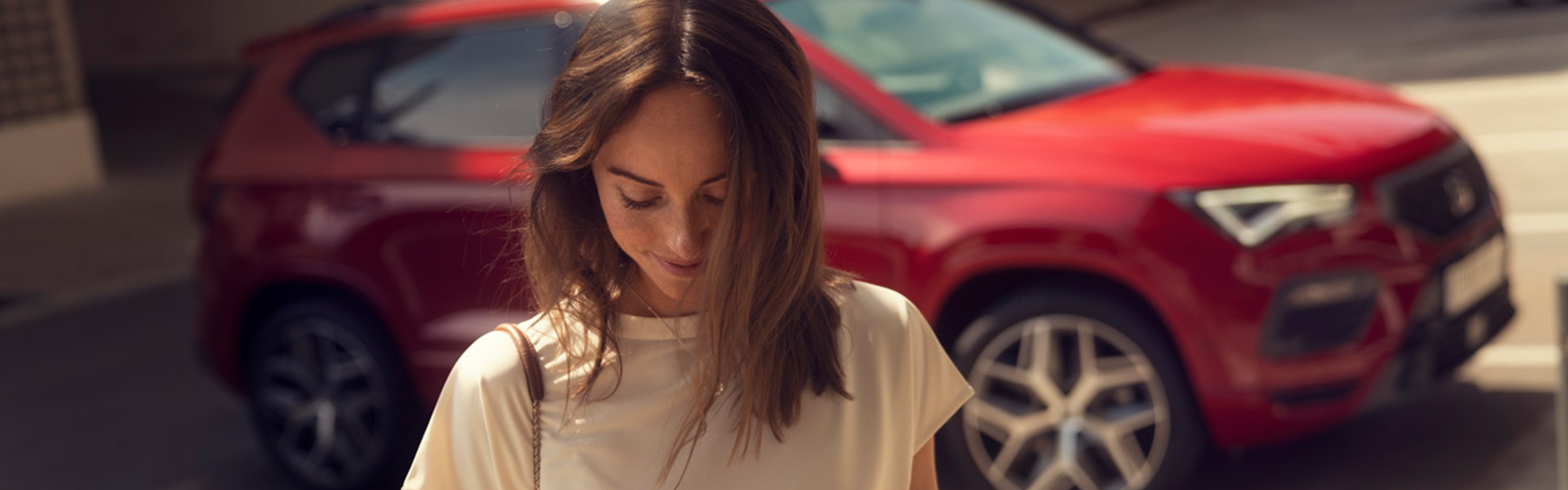 Vrouw staat voor een rode seat ateca en kijkt naar haar telefoon
