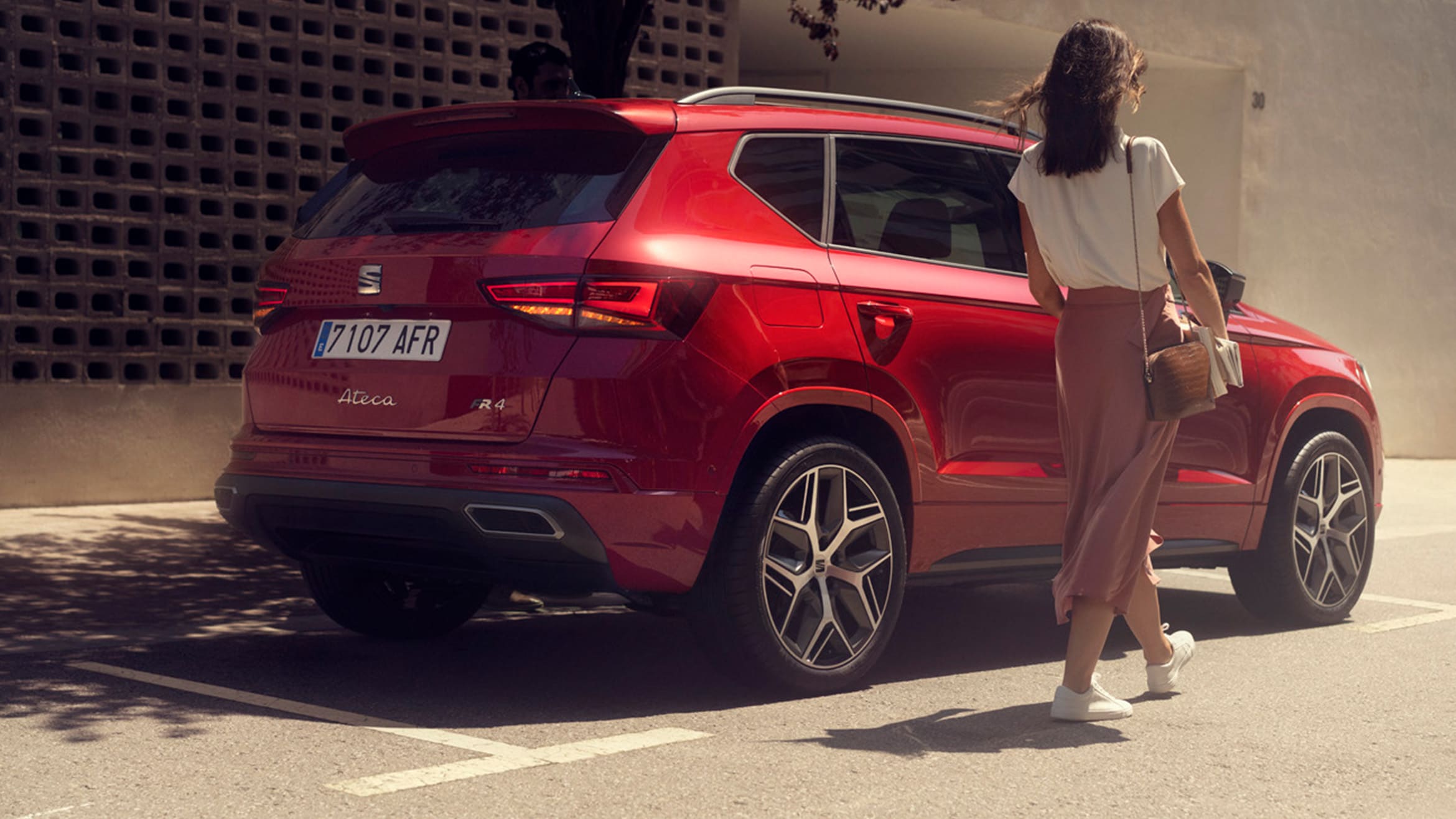 Vrouw in roze rok loopt naast een seat Ateca