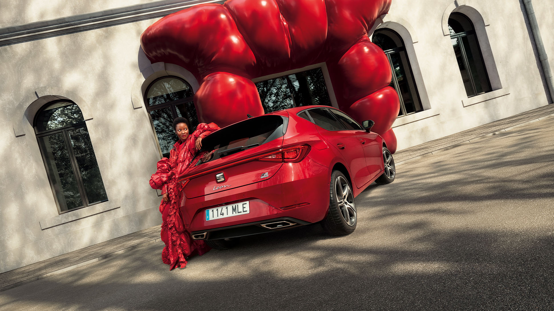 Vrouw met rood gewaad naast een rode SEAT Leon plug-in hybride