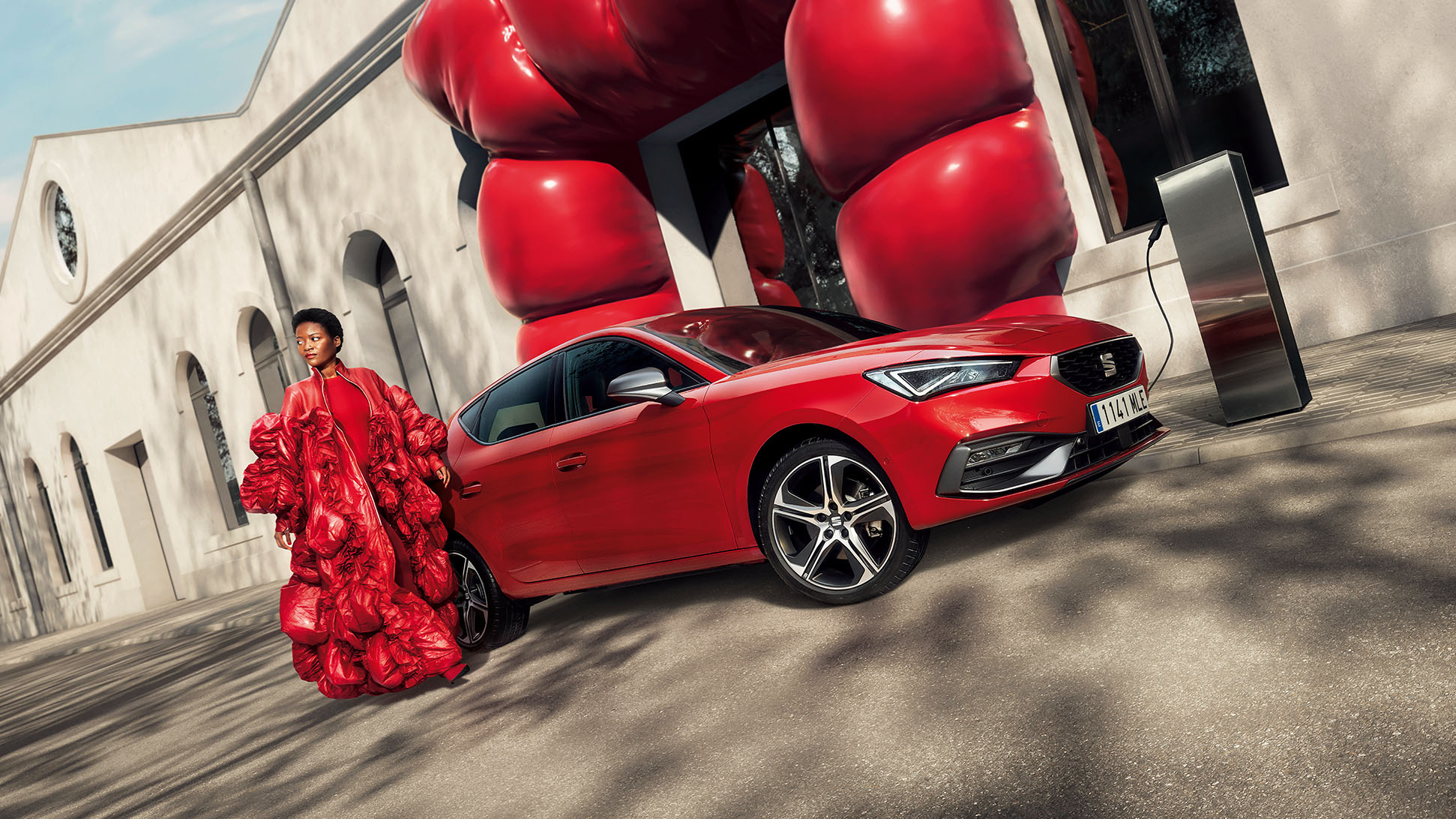 Vrouw met rood gewaad naast een rode SEAT Leon plug-in hybride aan de laadpaal