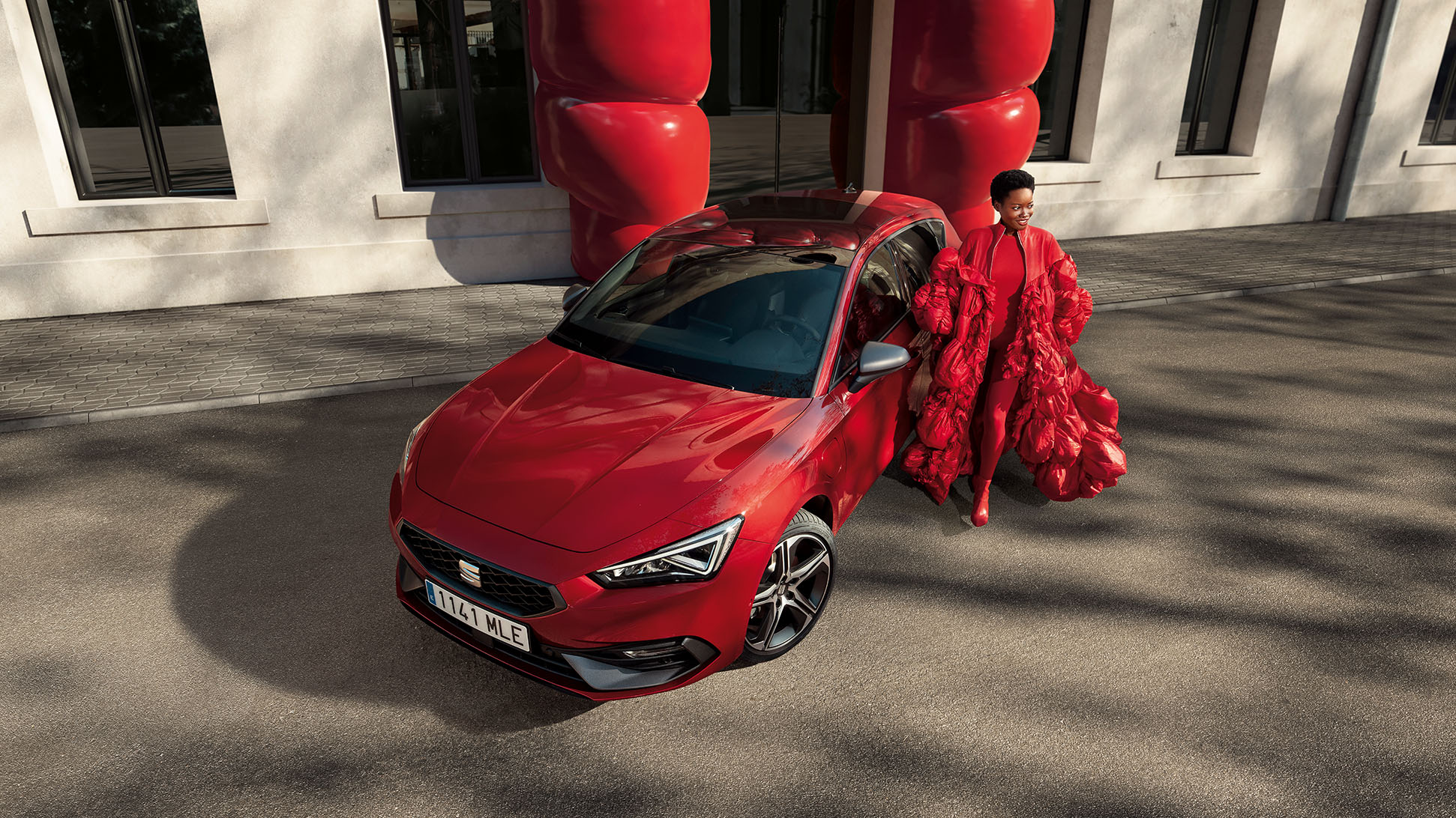 Vrouw met rood gewaad naast een rode SEAT Leon plug-in hybride aan de laadpaal