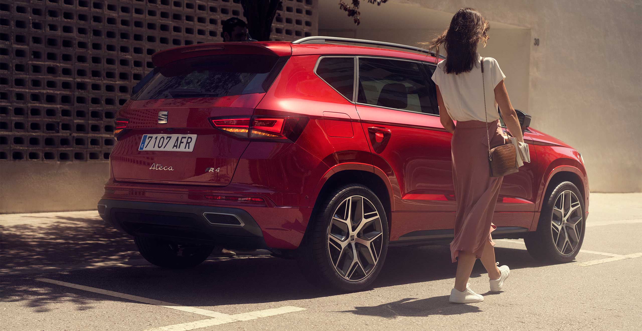 Vrouw in zomerse kleding loopt langs een rode SEAT Ateca FR