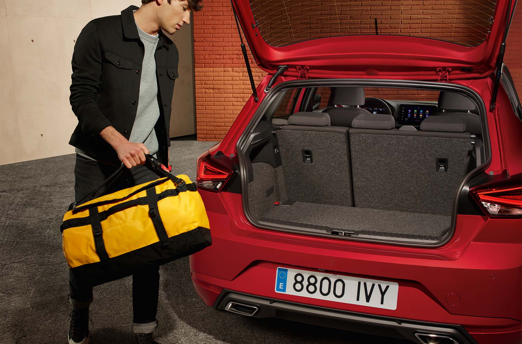 Man met gele tas naast rode SEAT Ibiza met open kofferbak