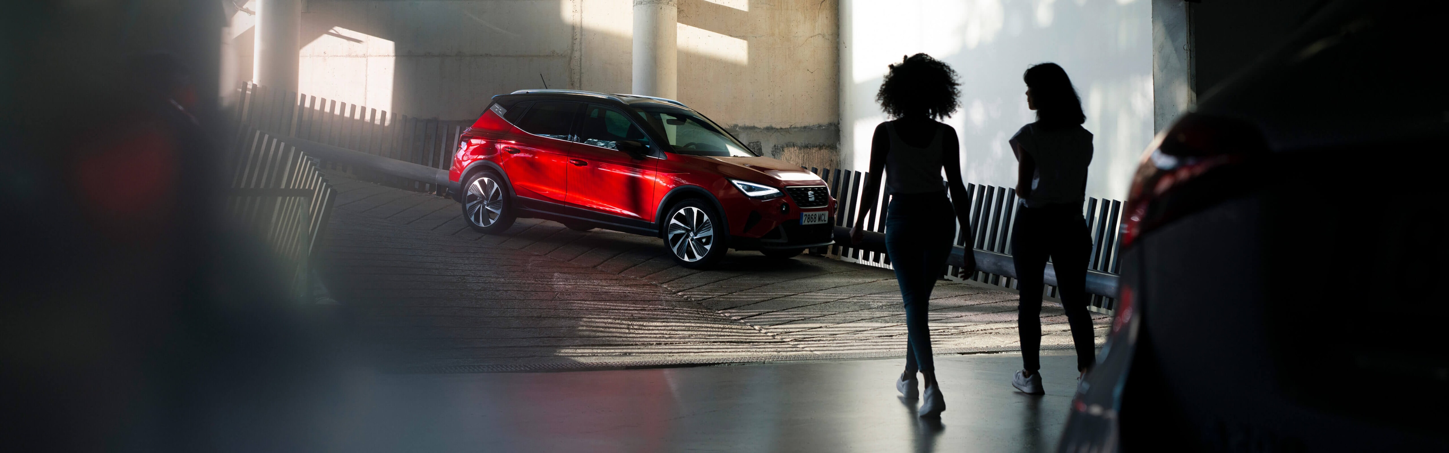 Twee vrouwen lopen in een parkeergarage richting een rode seat arona