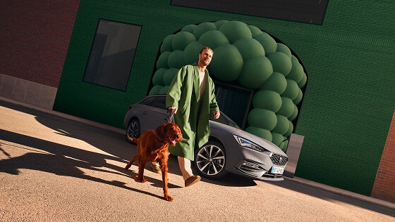 Man in een groene jas laat zijn hond uit en loopt langs een grijze seat leon sportstourer