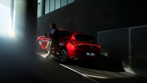 Man kijkt op zijn telefoon en leunt tegen een rode seat leon aan