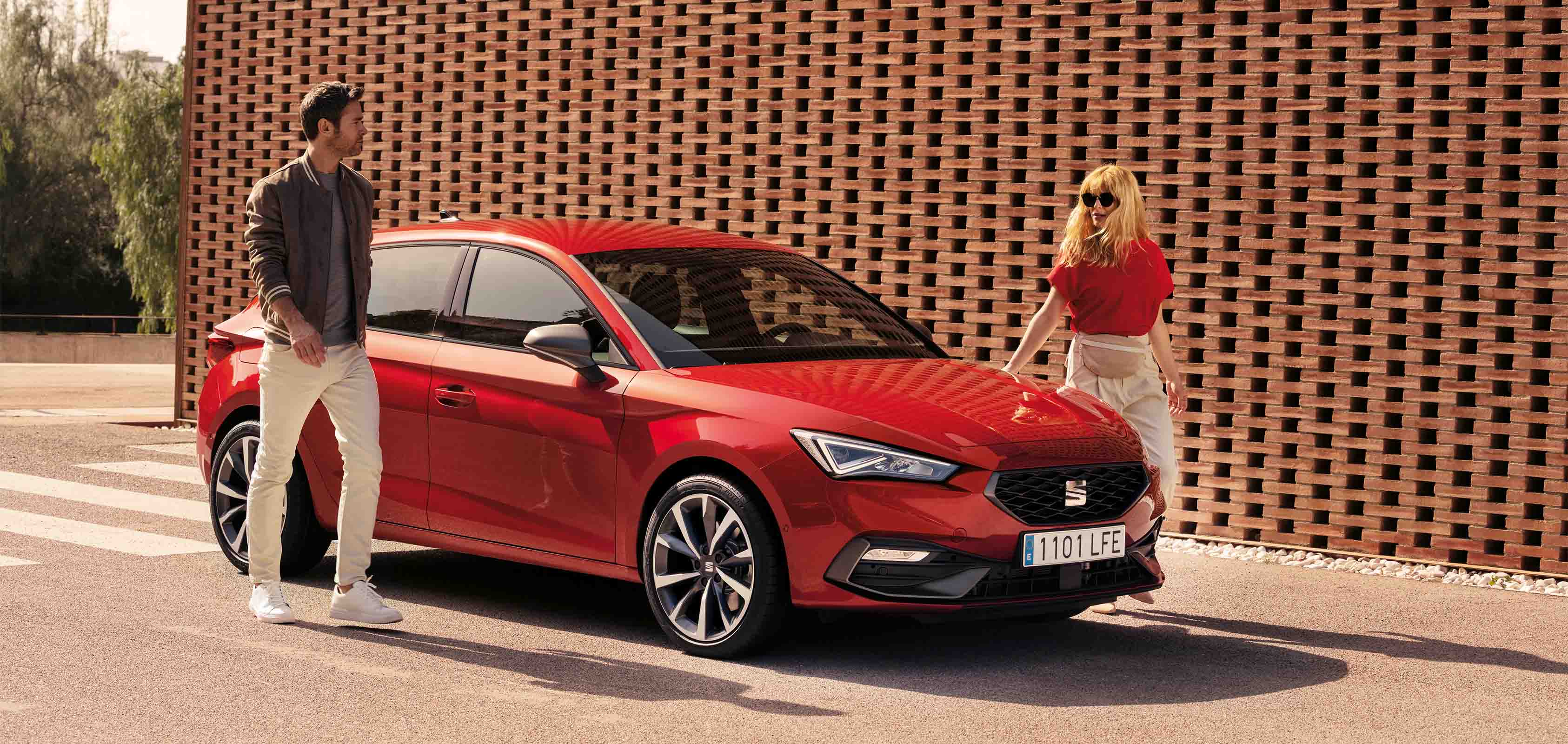 Man en vrouw lopen langs een rode SEAT Leon