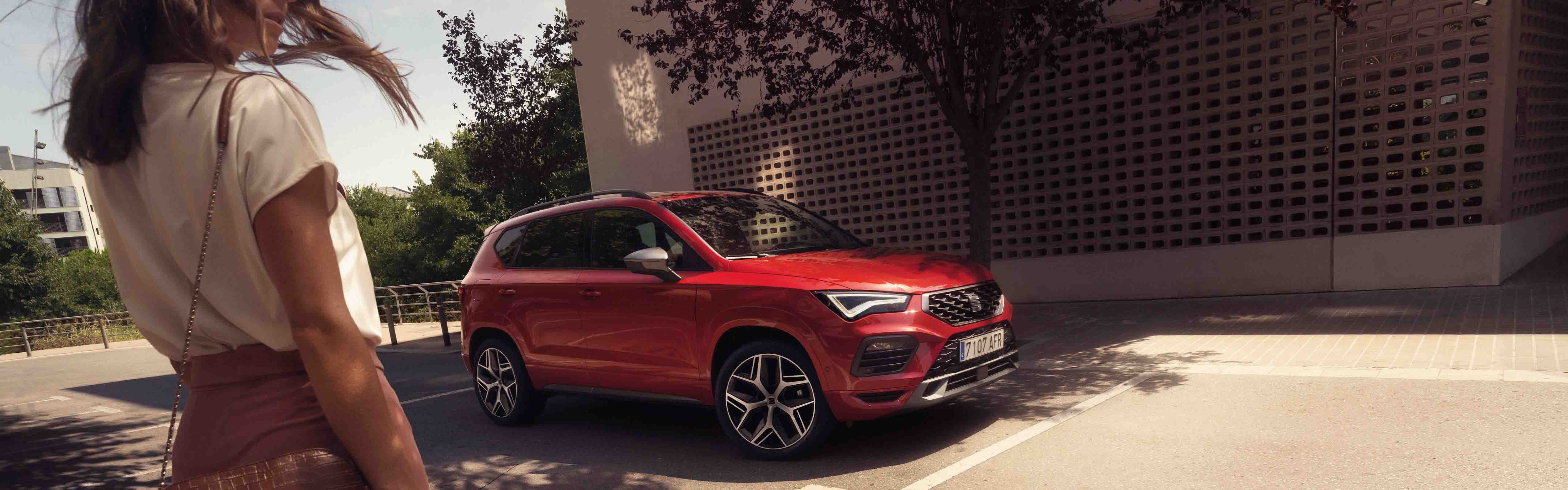 vrouw loopt naast een rode seat ateca geparkeerd langs de weg
