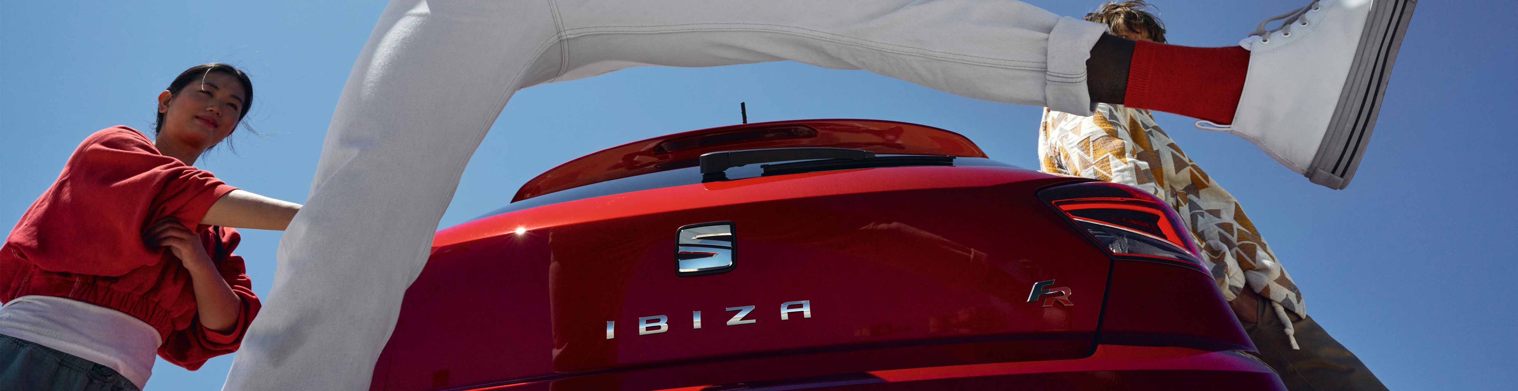 Vrouw staat bij een rode seat leon plug-in hybride en steekt de lader in de auto terwijl ze praat met een man