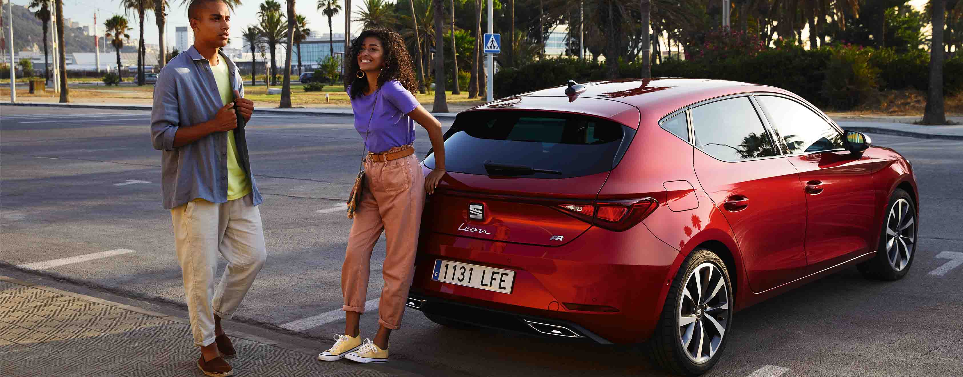 Een man en vrouw staan achter een seat leon FR in desire red
