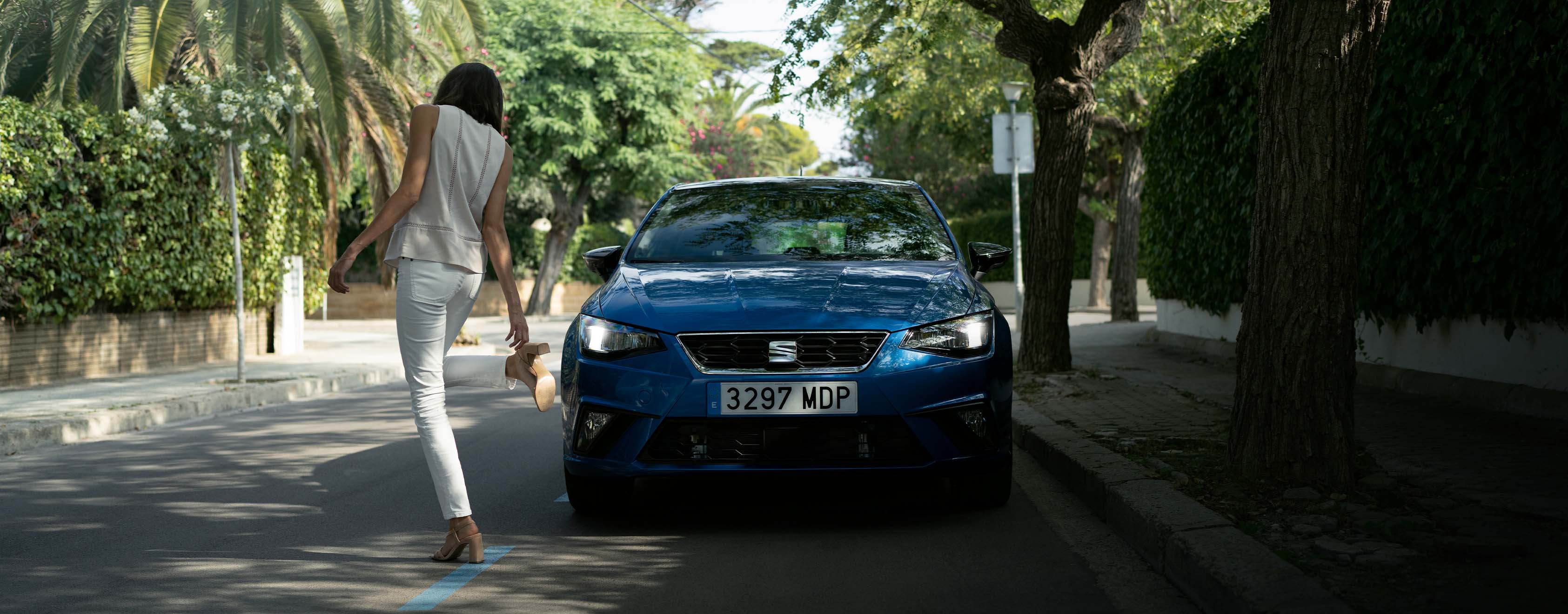 Vrouw pakt haar schoen vast voor een blauwe SEAT Ibiza die langs de straat geparkeerd staat