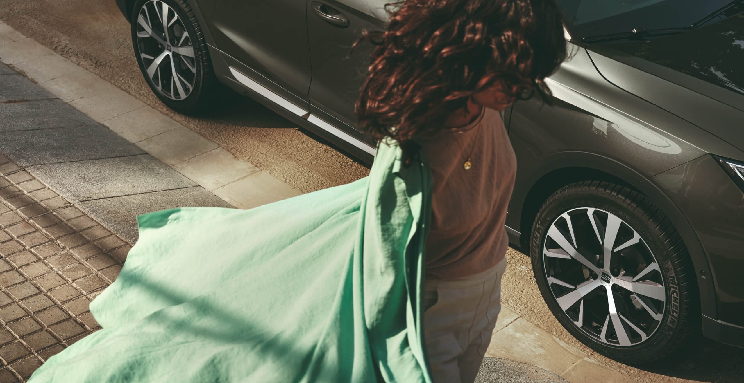 Vrouw met een wapperende groene jas staat naast een groene seat arona