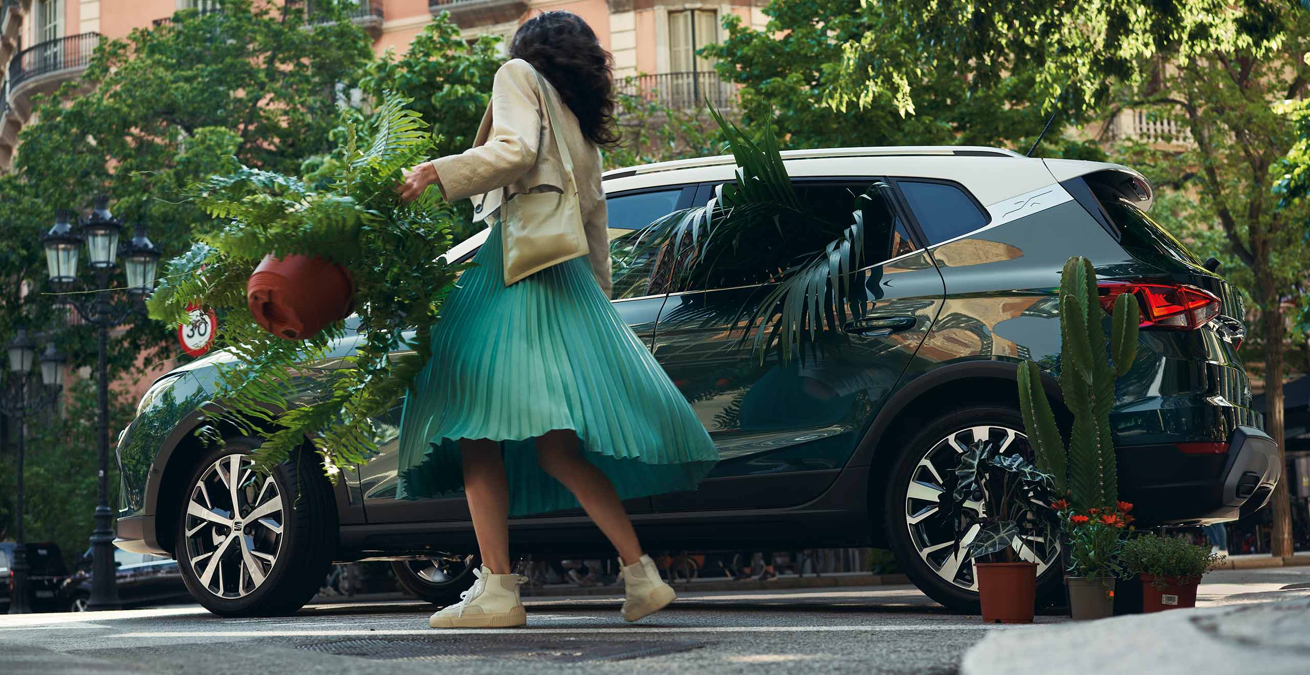 Vrouw met planten in haar handen, naast een groene SEAT Arona met daarin ook planten