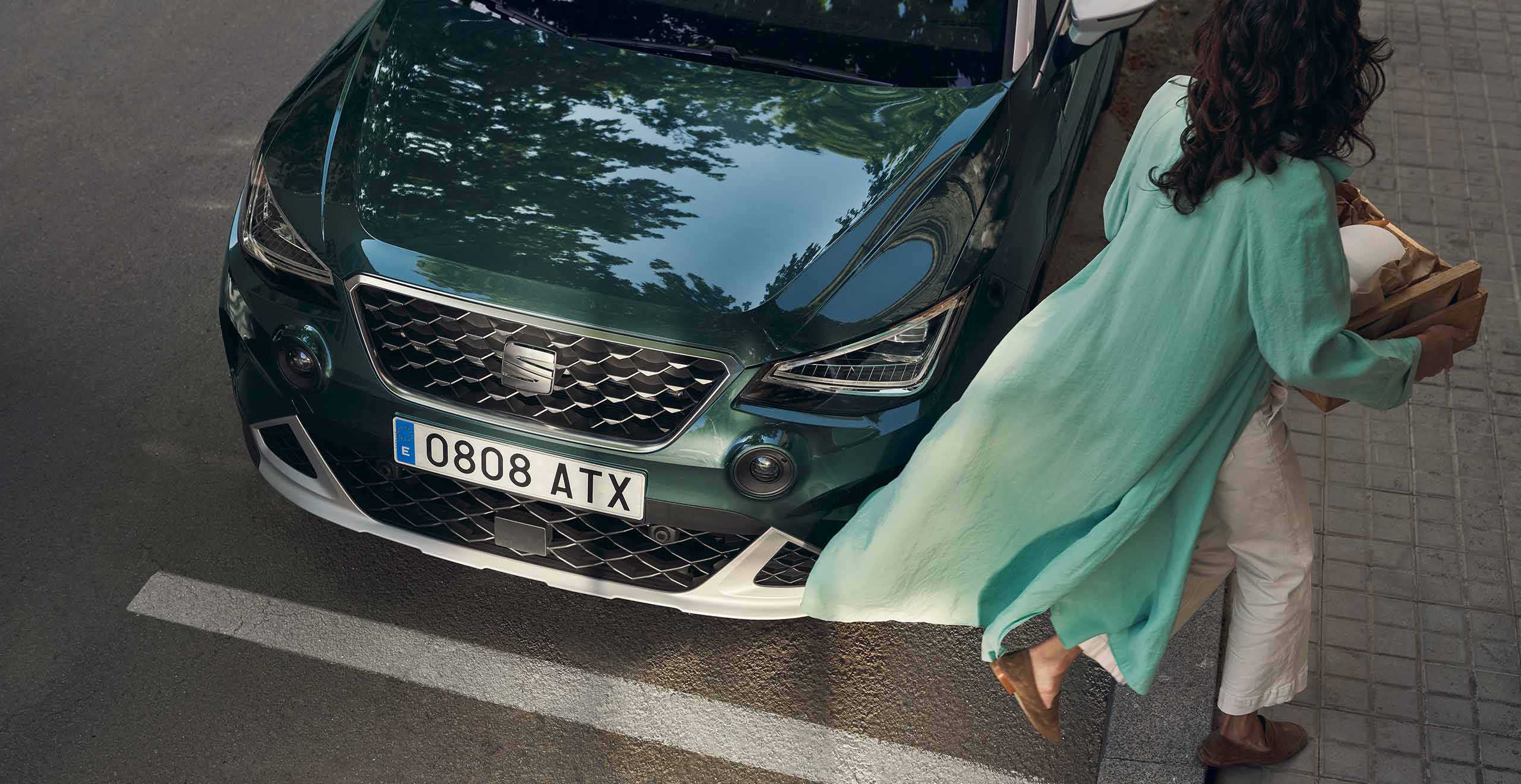 Vrouw in groen gewaad die langs een groene SEAT Arona loopt
