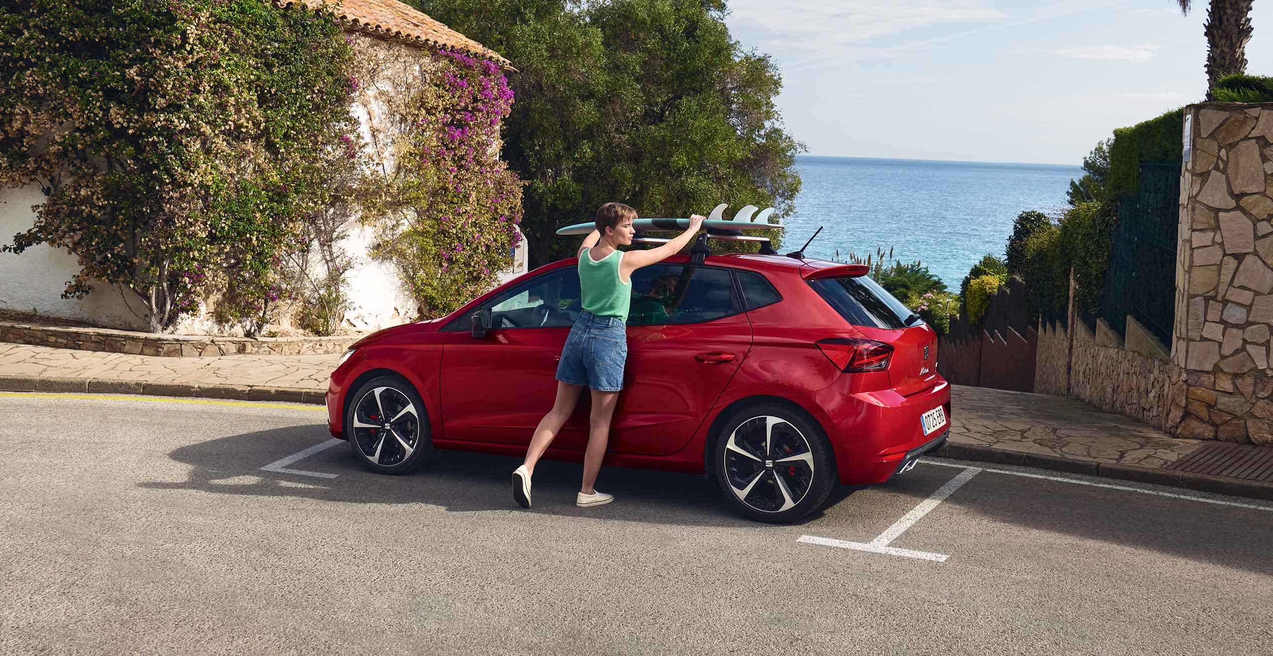 Vrouw die haar surfplank op een rode SEAT Ibiza monteert
