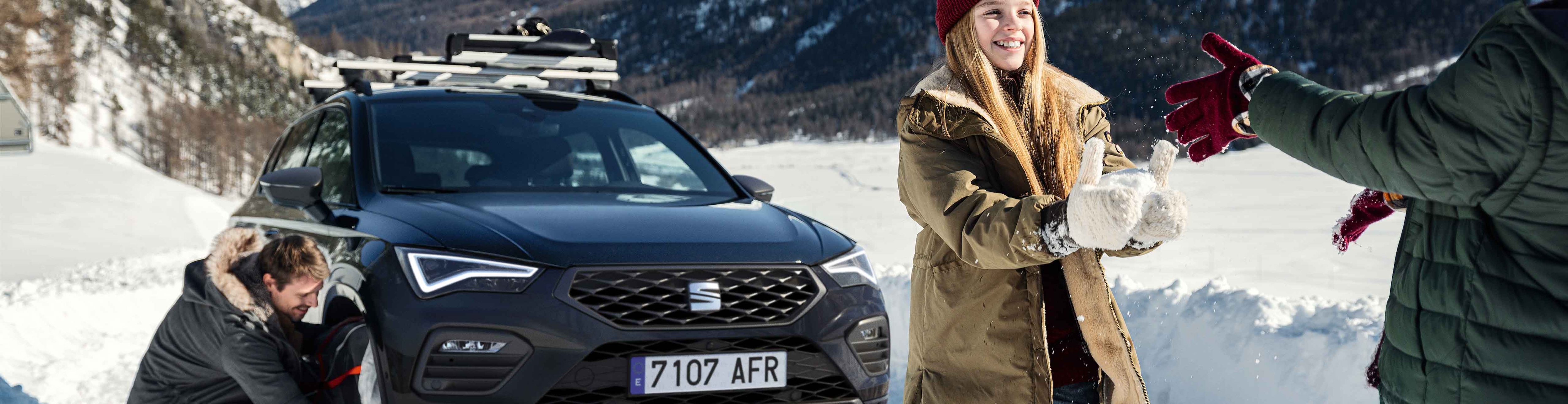 Meisje in de sneeuw naast een zwarte SEAT Ateca